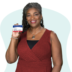African American woman in dark red dress holding her Medicare card and smiling.